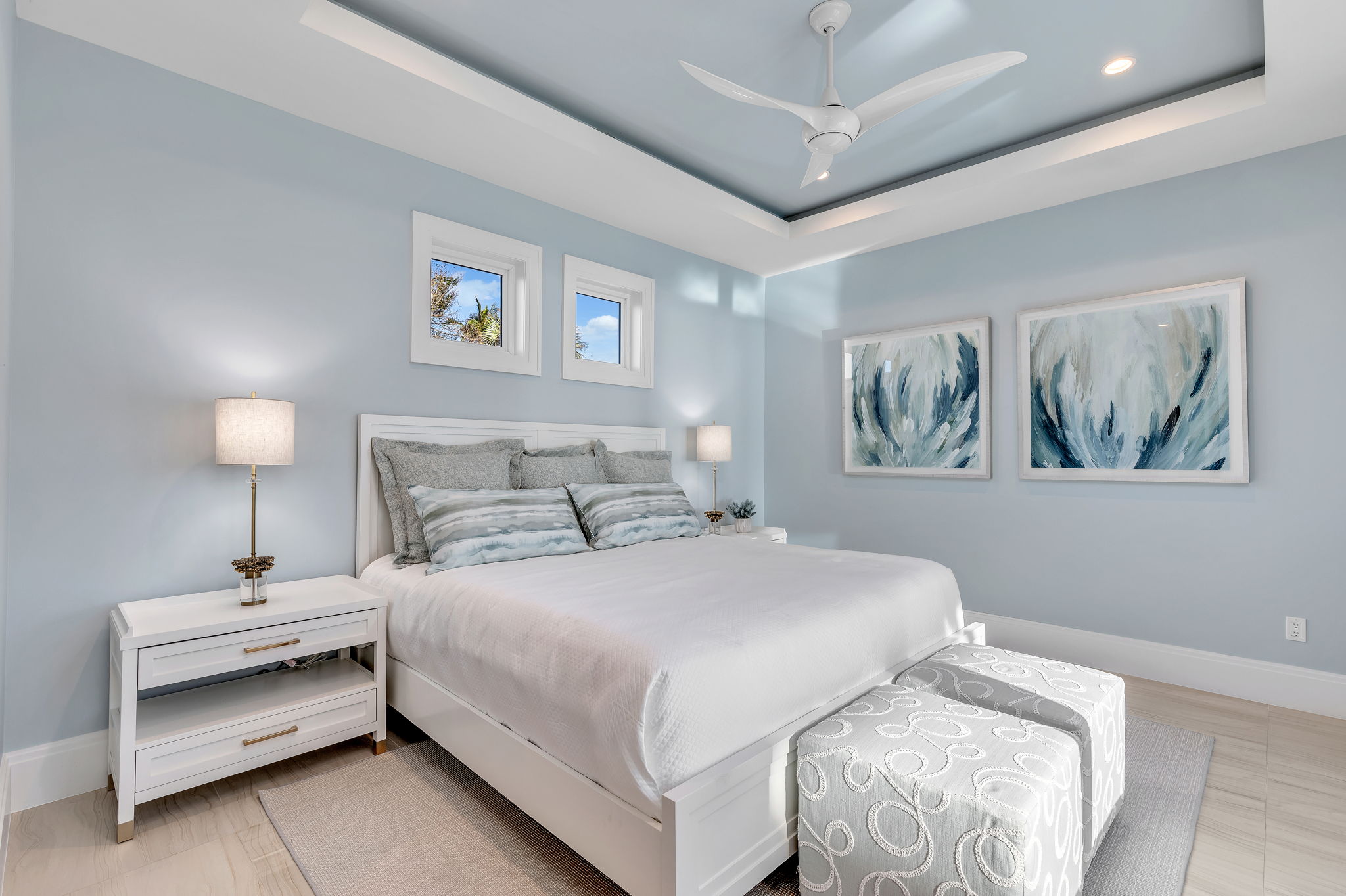 This bedroom features soft blue tones on the wall paint and step ceiling, as well as on some of the bedding pillows